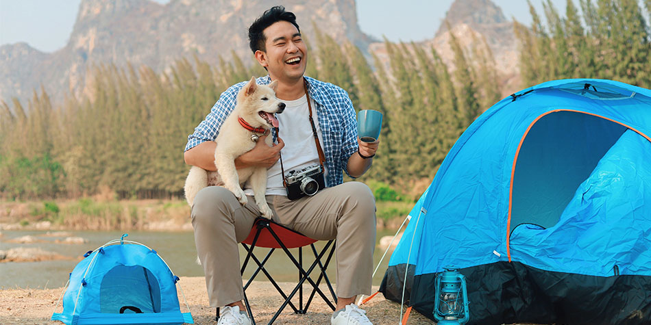 Man sitting in front of a tent with a dog in his lap.