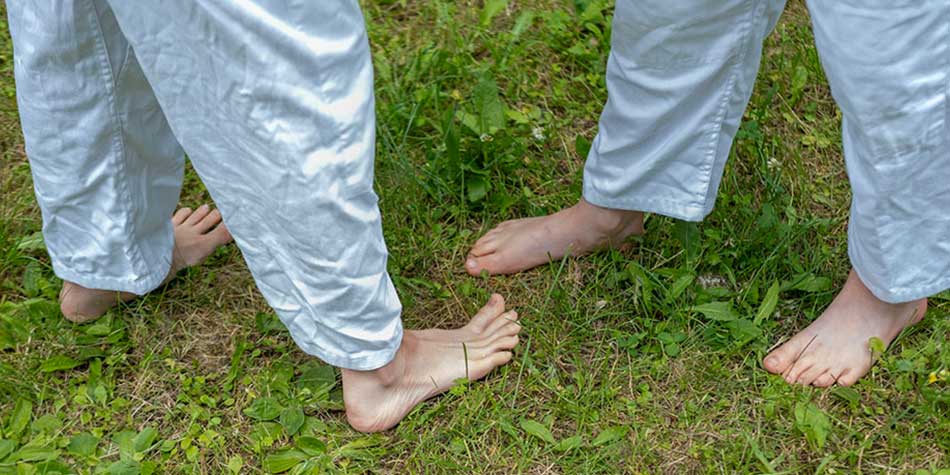 Photo of the feet of two people standing barefoot in a field of grass.