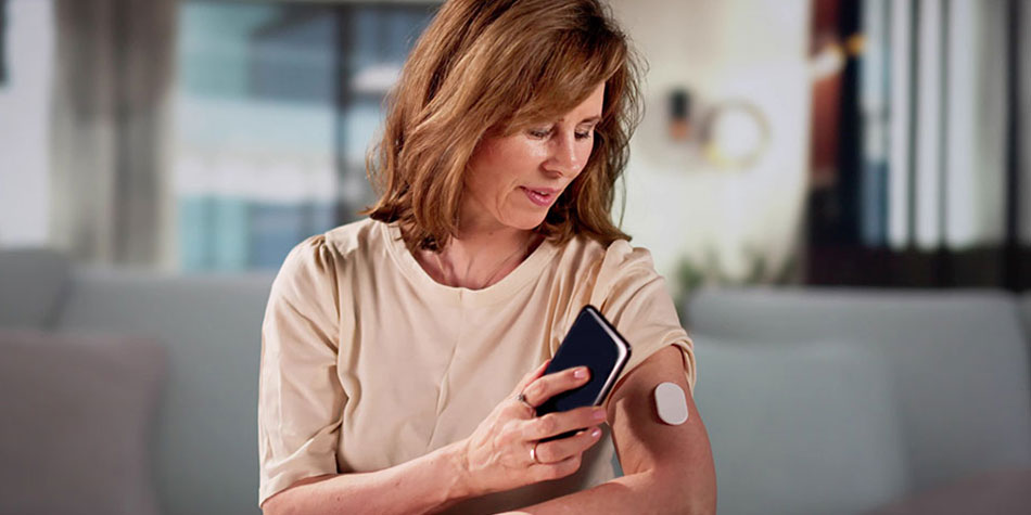 Woman checking her glucose levels using her phone and a device in her arm.
